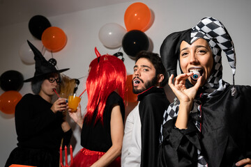 Halloween party at home. Devil, witch, dracula and harlequin posing and having fun