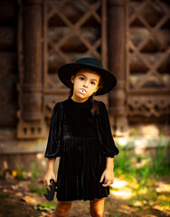 little girl, in a black dress and hat,with vampire teeth for halloween