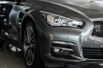 Front right modern headlight on luxury silver new car in automobile salon. Detail grey metallic...