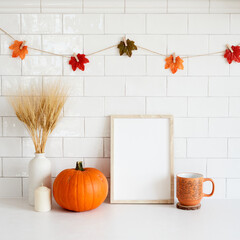 Mockup frame with pumpkin, candle, coffee cup, vase of wheat in cozy home interior with autumn fall decorations. Thanksgiving, Halloween holiday poster design.