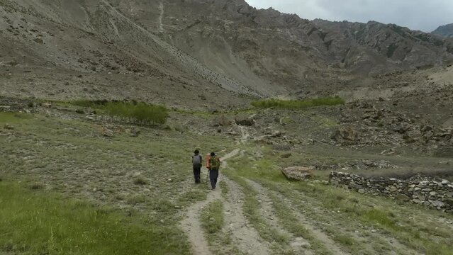 Drone flights in the back of  3 people walking in a green area in the mountains, filmed close to Khalpu in Pakistan