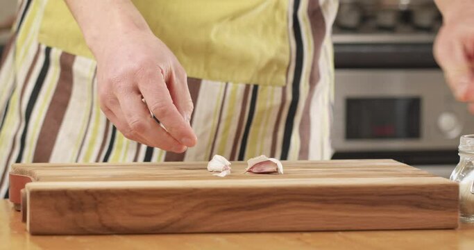 Male home cook crushing a garlic clove on a cutting board in his kitchen. Closeup shot.