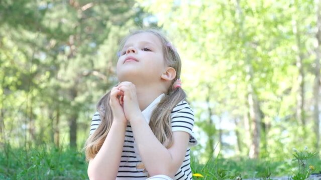 Little girl praying outdoors, hands folded in prayer. Faith, spirituality, wishing and hope concept
