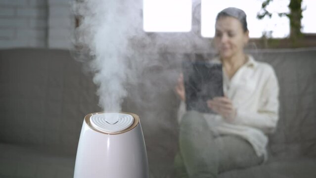 Woman comfort with aroma diffuser in room. A woman relax in comfort with her smartphone against new smart air humidifier in the room.