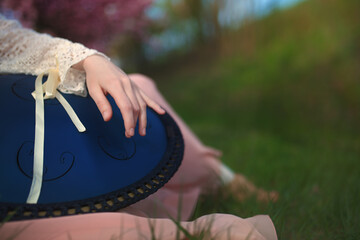 Female hand playing a tongue drum musical instrument (metal drum with cut steel tongues and a unique sound). It is very similar to the musical instrument called a handpan, hang or pantam.