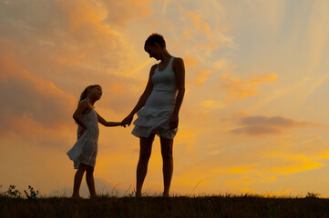 Silhouette of mother and daughter on the summer meadow during sunset