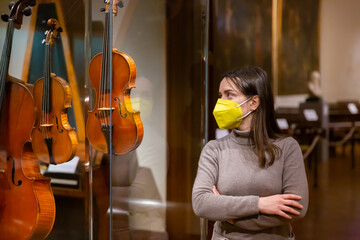 Interested young woman wearing protective face mask viewing collections of ancient musical...