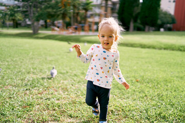 Little girl walks on the green grass with her tongue out. High quality photo