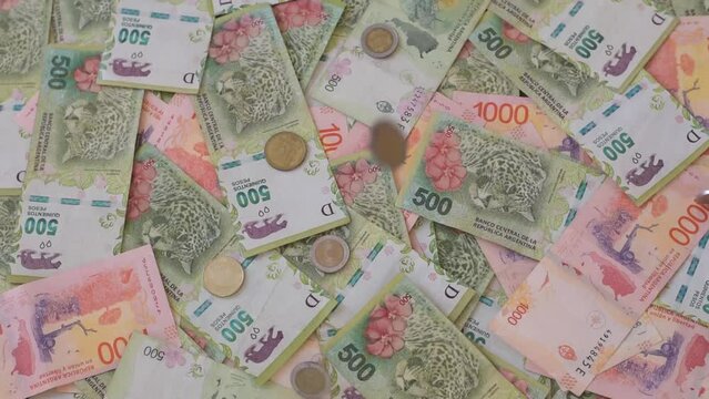 monedas cayendo sobre un colchon de billetes de 500 y 1000 pesos argentinos