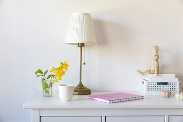 White floor lamp with lampshade. A pink notebook with springs, a white coffee mug, a wooden toy...