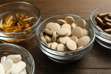 Different dietary supplements in glass bowls on wooden table, closeup