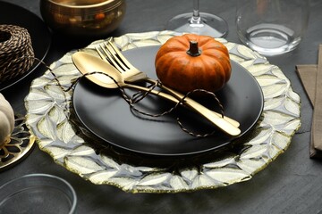 Autumn table setting with golden cutlery and pumpkin on black background