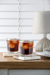 Glasses of cold drink with stylish cup coasters, lamp and stationery on wooden table in room