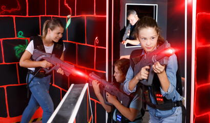 Fototapeta na wymiar Fine girl aiming laser gun at other players during laser tag game in dark room