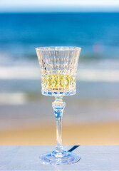 A glass of white wine close-up on the background of the beach. The background is blurry.