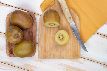 Kiwi sliced and whole fruits on cutting board with knife. On  white table.