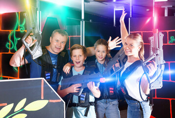Group of happy glad positive teenagers and adults with laser guns posing together while having fun on lasertag arena