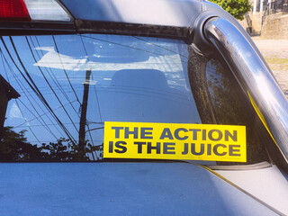Encouraging bumper sticker message on a car window that says "The Action is the Juice"