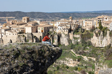 Fototapeta na wymiar Young female tourist with a camera, climbing on top of a cliff, photographs a picturesque landscape with a view of the city ..of Cuenca, Spain