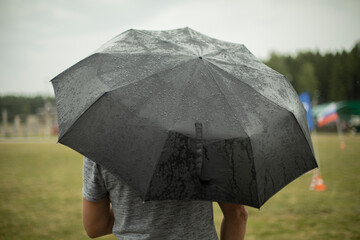 Black umbrella in rain. Large umbrella in bad weather. Man on street on cloudy day.
