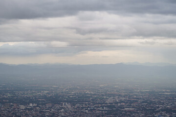 Top view of mountain in Chiang Mai City, Thailand. White cloud and dust is above of the mountain while cities can be seen far away.