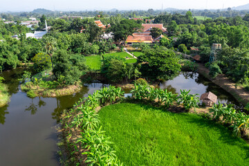 Fototapeta na wymiar Drone view of Sufficiency Economy, Land full of agricultural activities with green rice fields, big ponds, and trees. Small houses and temple close by a pond.
