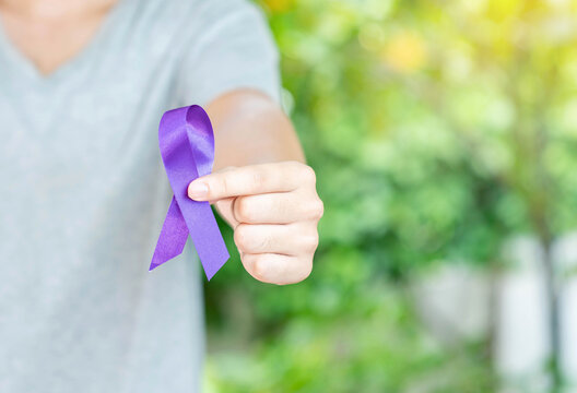 The man in grey shirt show purple in hand on out of focus background.