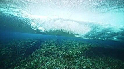 Underwater shot of blue barreling wave with silhouette of surfer in the barrel riding in slow motion. Tahiti famous surf destination for surfers, French Polynesia. 