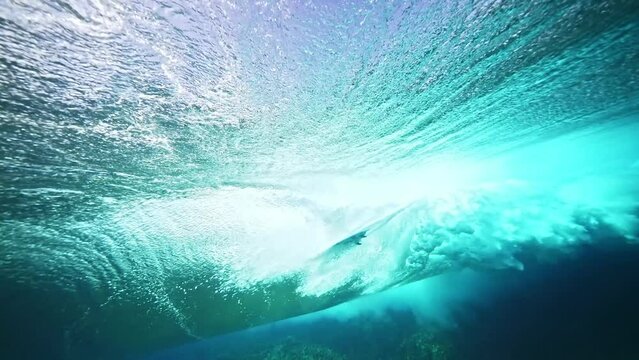 Underwater shot of surfer silhouette riding in huge blue ocean wave. 4k slow motion. Teahupoo famous action sports destination in Tahiti. travel in French Polynesia. 