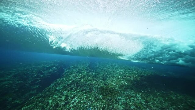 Underwater shot of blue barreling wave with silhouette of surfer in the barrel riding in slow motion. Tahiti famous surf destination for surfers, French Polynesia. 