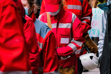 A crowd of emergency medic assistants in red uniforms with helmets stands outdoors. Paramedic. Patient. Person. Profession. Red. Rescue. Rescuer. Safety. Sick. Street Girls. Uniform. Female