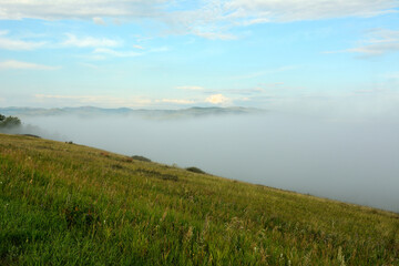 Obraz premium View from the top of a high hill to the valley completely hidden by dense fog.