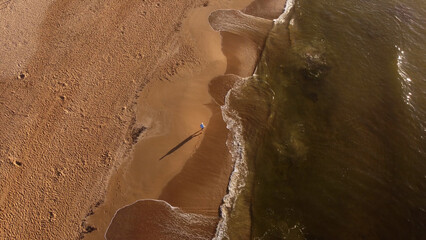 Aerial top down view of person walking on the beach at Punta del Este Uruguay. Wave and foam at sunrise.