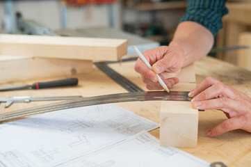A carpenter measures wooden planks and makes marks with a pencil in a workshop.