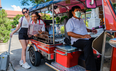 Obraz premium Two young European girl travelers get information and bargain the tuk tuk taxi rate for travelling around Chiang Mai downtown. Transportation concept.