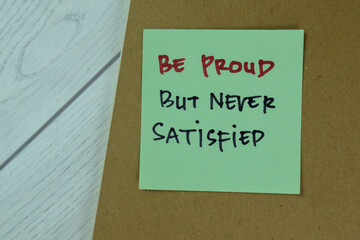 Concept of Be Proud But Never Satisfied write on sticky notes isolated on Wooden Table.