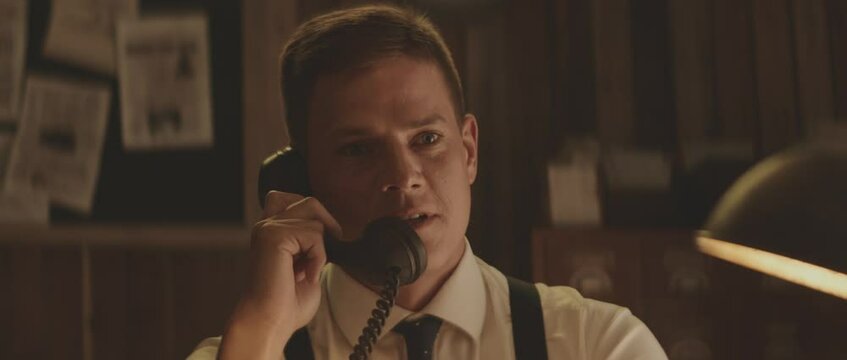 Cheerful man in formal clothes speaking to old telephone handset. Retro style detective using deduction for solving challenging cases.