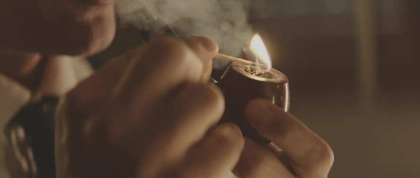 Detailed view of man while lighting his pipe. Retro style detective using deduction for solving challenging cases.