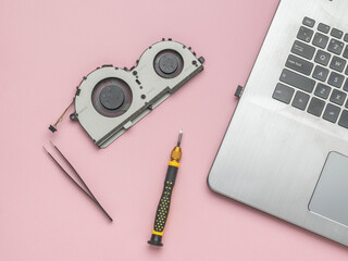 A screwdriver, a laptop cooler and an open laptop on a pink background.