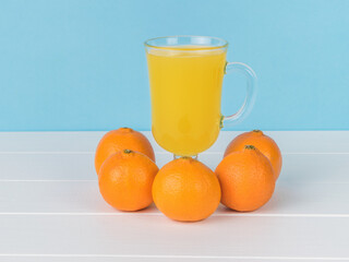 Five tangerines and a glass glass with juice on a white table.