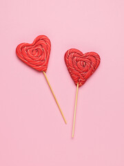 Red candy on sticks in the shape of a heart on a pink background. Minimal concept of sweet life and love.