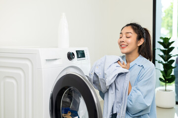 Happy housewife opens the front of the washing machine and smiles to receive the laundry that has...