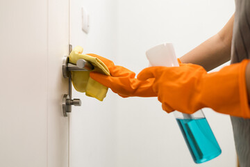 Close up hand of housewife with rubber gloves using spray bottle and microfiber towel to clean door...