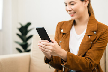 Beautiful young women using mobile phone sitting on sofa in living room. Using smartphone. Woman Shopping online store. Relax time at home