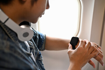 Young Asian male passenger looking at his wristwatch, checking the landing time. cropped image
