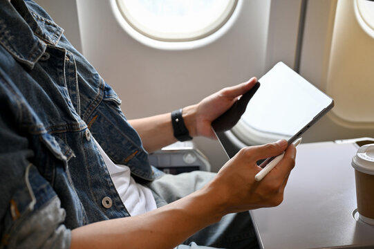 Male traveler passenger using his digital tablet during the flight on a plane. cropped image