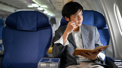 Smart Asian businessman on the plane, planning his business while looking out the window.