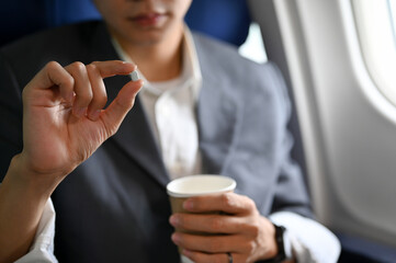 A male passenger holding a cup of water and an airsick motion sickness pills. - obrazy, fototapety, plakaty