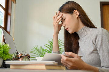 Stressed young Asian female suffering from headache or migraine during work