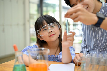 Asian girl with science goggles learning and doing fun science experiment with her teacher.